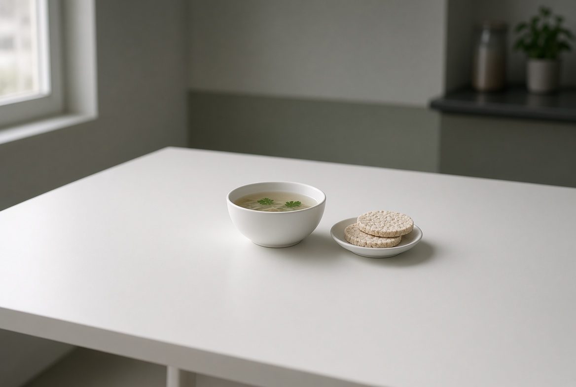 Small bowl of thin broth and two rice cakes on an otherwise empty table